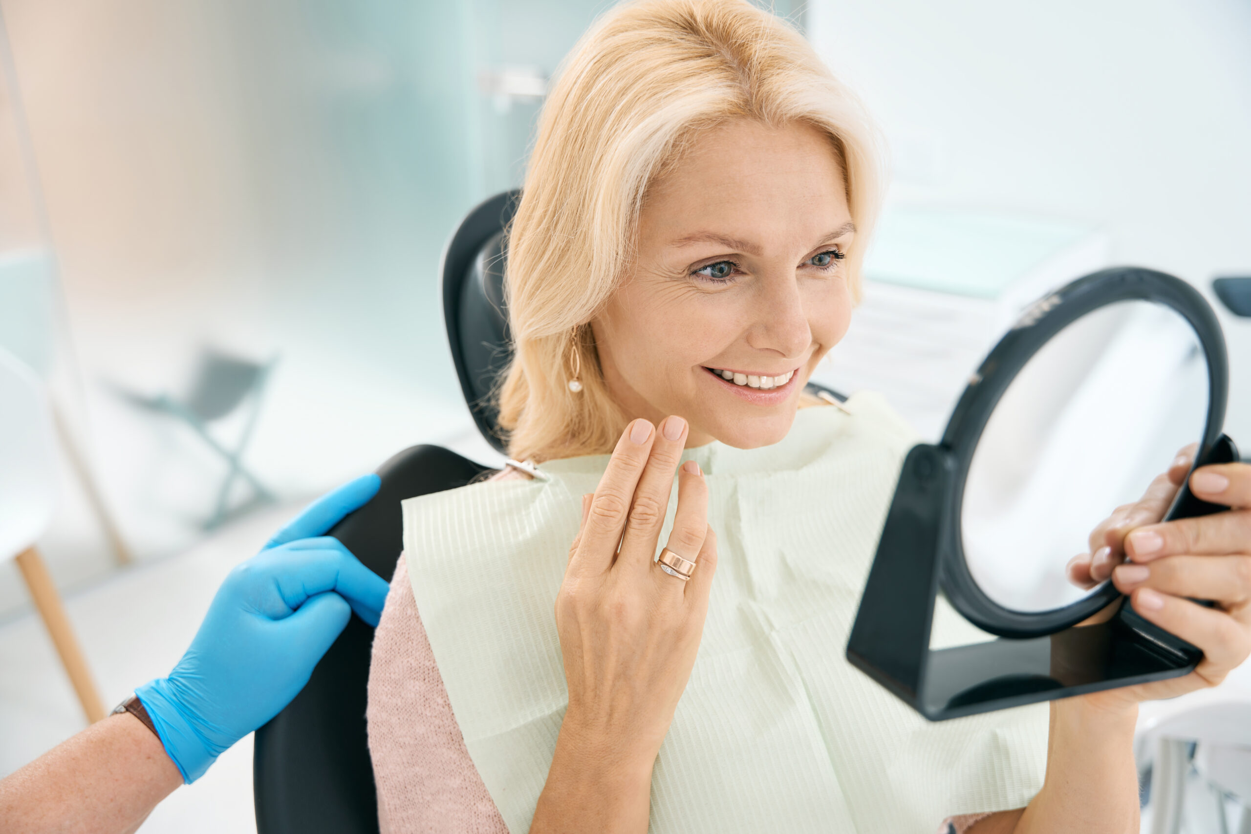 Smiling woman looking at her teeth in a mirror at the dentist